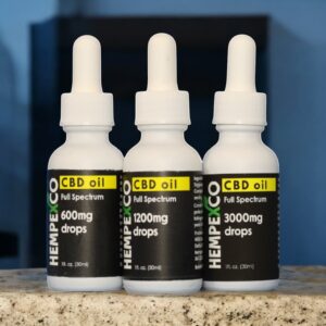 Full Spectrum Hemp oil shown on a concrete countertop in white bottles with black and yellow labels