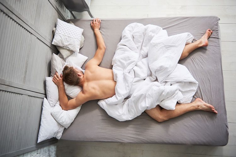Man laying face down in bed with white sheets for article Best CBD for Sleep